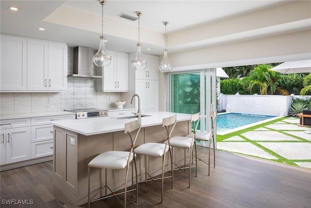 kitchen featuring a kitchen breakfast bar, white cabinetry, a kitchen island with sink, and wall chimney exhaust hood