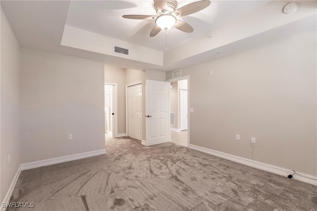 unfurnished bedroom with light carpet, a closet, a tray ceiling, and ceiling fan