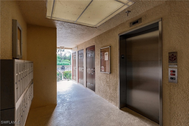 corridor with a textured ceiling, elevator, a mail area, and light colored carpet