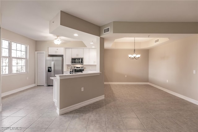 kitchen with kitchen peninsula, appliances with stainless steel finishes, ceiling fan with notable chandelier, pendant lighting, and white cabinetry