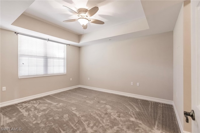 carpeted spare room featuring a raised ceiling and ceiling fan