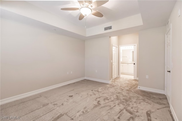 empty room with ceiling fan, a raised ceiling, and light carpet