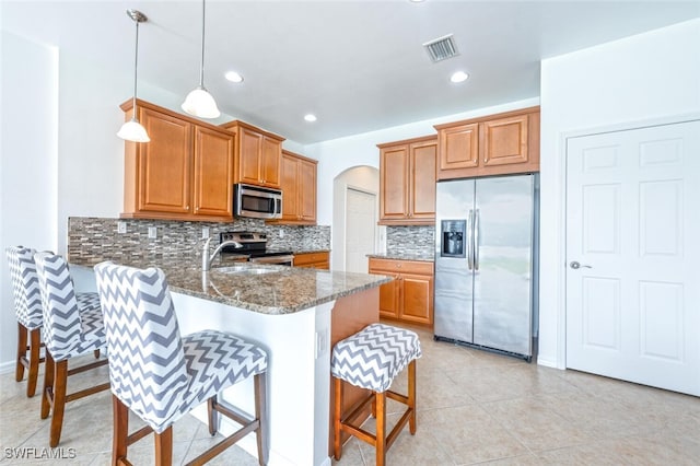 kitchen with sink, hanging light fixtures, dark stone countertops, appliances with stainless steel finishes, and kitchen peninsula