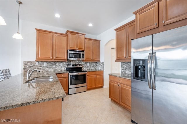 kitchen featuring backsplash, light stone counters, stainless steel appliances, sink, and decorative light fixtures