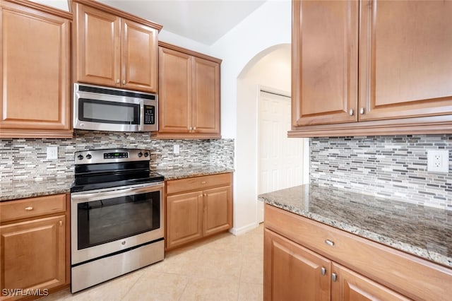 kitchen with backsplash, stainless steel appliances, light stone counters, and light tile patterned flooring