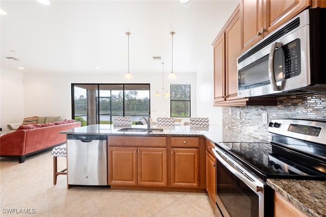 kitchen with backsplash, sink, hanging light fixtures, stone countertops, and stainless steel appliances