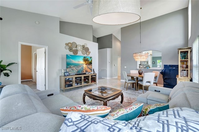 tiled living room with ceiling fan with notable chandelier and high vaulted ceiling