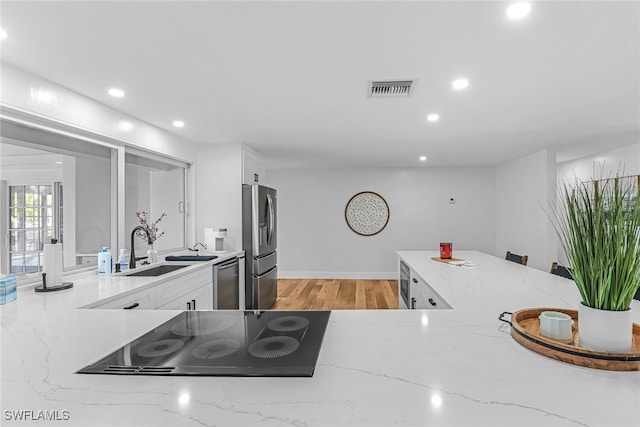 kitchen with a sink, stainless steel appliances, light stone counters, visible vents, and white cabinetry