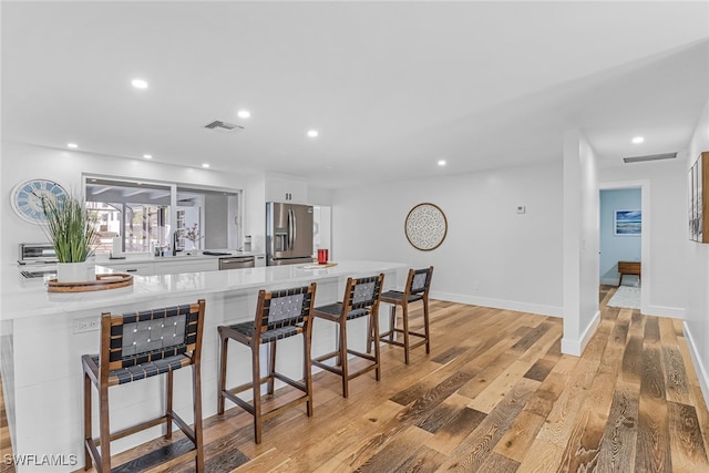 kitchen with light countertops, a breakfast bar area, white cabinetry, light wood-style floors, and stainless steel appliances