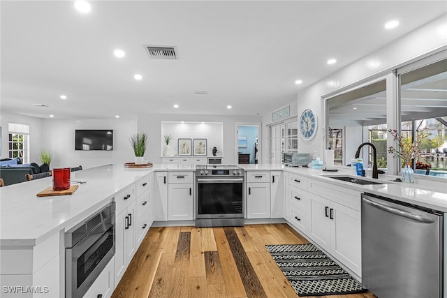 kitchen with appliances with stainless steel finishes, light stone counters, visible vents, a sink, and light wood-type flooring