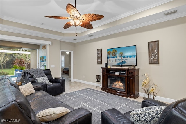 living room featuring a raised ceiling, ceiling fan, and ornamental molding