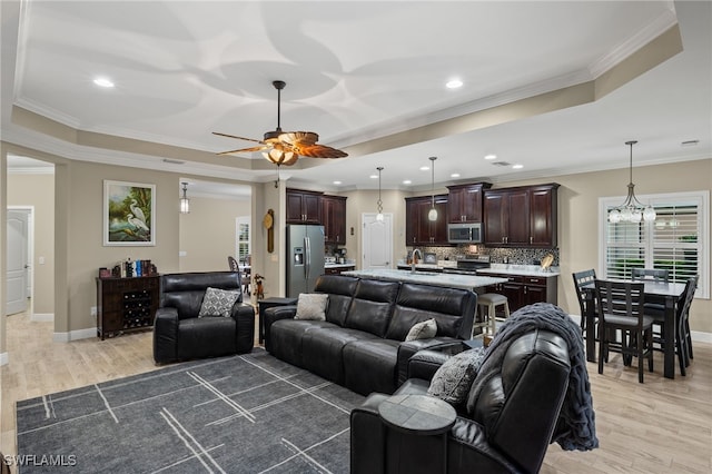 living room with a tray ceiling, light hardwood / wood-style floors, ceiling fan with notable chandelier, and ornamental molding