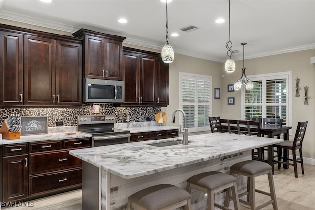 kitchen featuring sink, hanging light fixtures, stainless steel appliances, an island with sink, and a breakfast bar