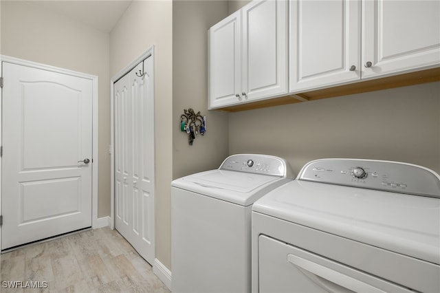 clothes washing area featuring cabinets, washer and dryer, and light hardwood / wood-style floors