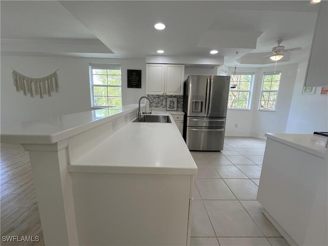 kitchen featuring stainless steel fridge, a peninsula, a tray ceiling, light countertops, and a sink