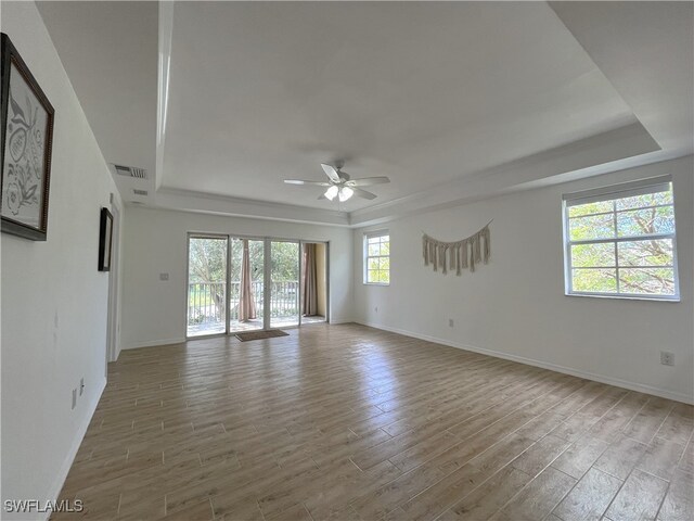 spare room with light wood-type flooring, a tray ceiling, a wealth of natural light, and ceiling fan