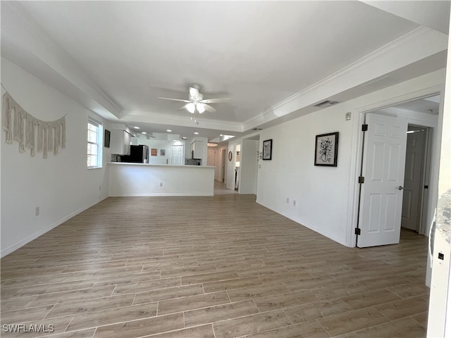 unfurnished living room featuring a tray ceiling, ceiling fan, crown molding, and light wood-type flooring