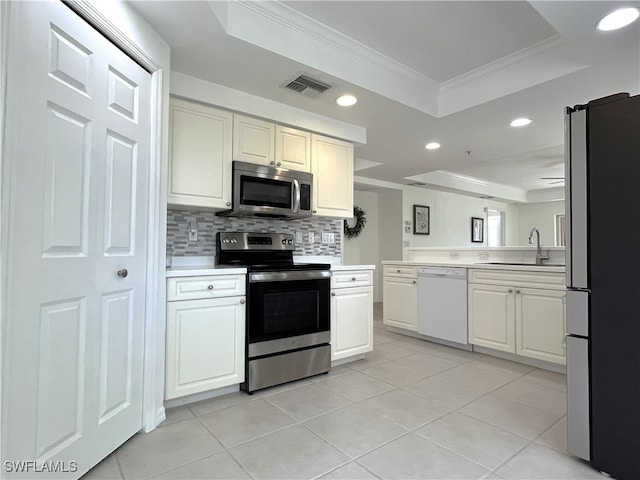 kitchen with stainless steel appliances, a tray ceiling, crown molding, sink, and light tile patterned floors