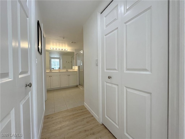 hall with light wood-style floors, baseboards, and a sink