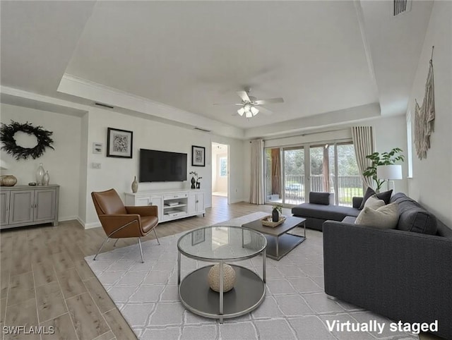 living area with light wood-type flooring, visible vents, and a tray ceiling