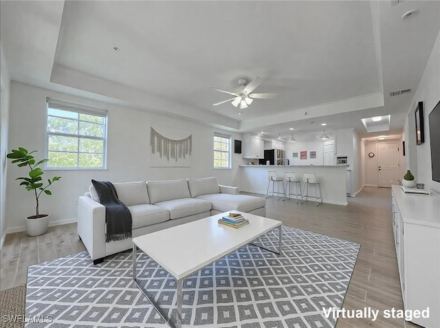 living area featuring baseboards, visible vents, a raised ceiling, and wood finish floors