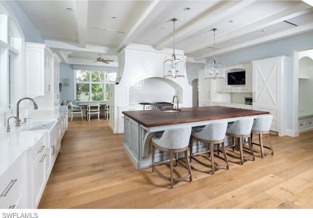 kitchen featuring butcher block countertops, white cabinetry, a kitchen island with sink, and light hardwood / wood-style flooring