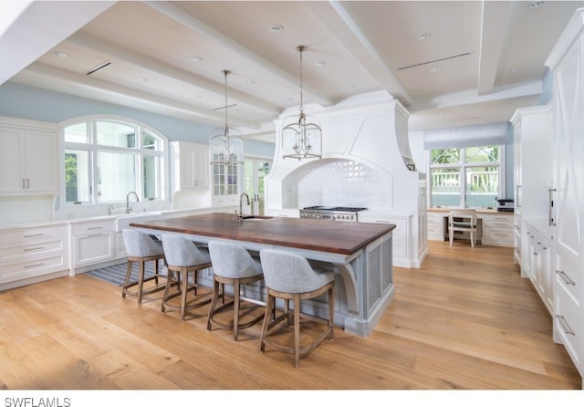 kitchen featuring sink, light hardwood / wood-style flooring, butcher block countertops, decorative light fixtures, and white cabinets