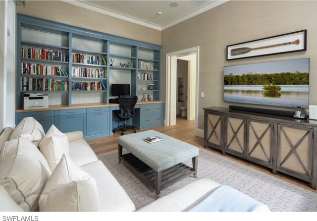 living room with built in shelves, crown molding, built in desk, and light wood-type flooring