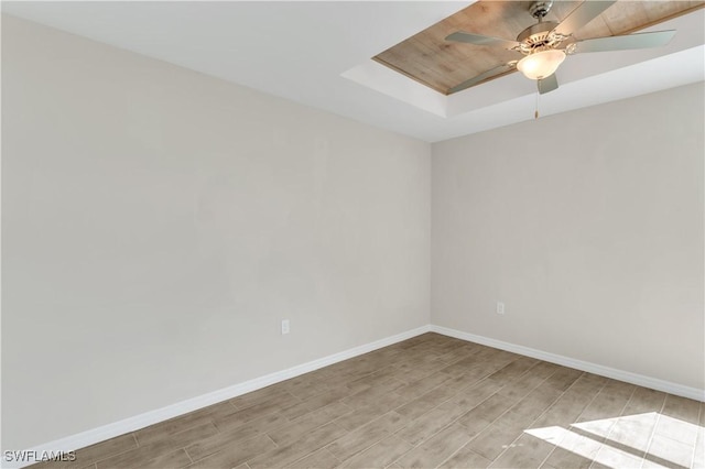 unfurnished room featuring a raised ceiling, ceiling fan, and light hardwood / wood-style floors