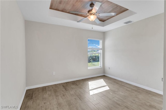 empty room featuring a raised ceiling, ceiling fan, light hardwood / wood-style flooring, and wooden ceiling