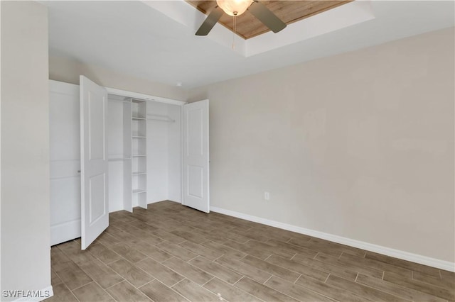 unfurnished bedroom with ceiling fan, a tray ceiling, and a closet