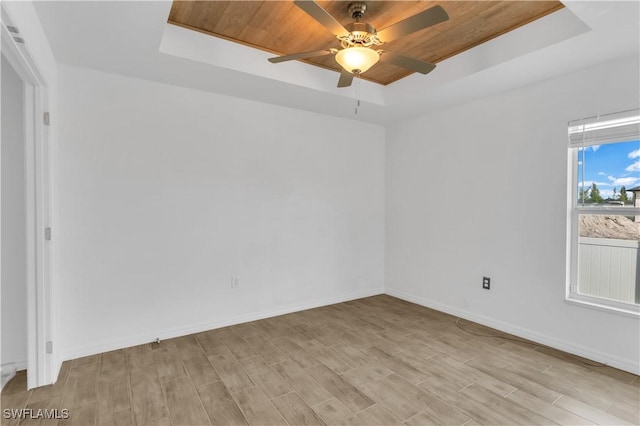 empty room with a raised ceiling, light wood-type flooring, and wooden ceiling