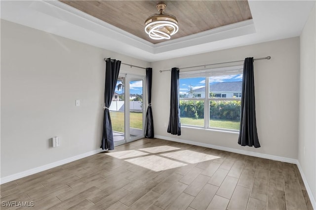 empty room with a tray ceiling, ornamental molding, wood ceiling, and light wood-type flooring