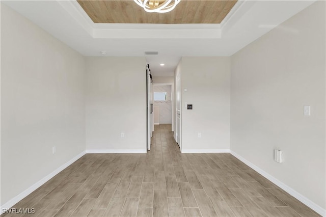 spare room featuring a barn door, a tray ceiling, and light hardwood / wood-style floors