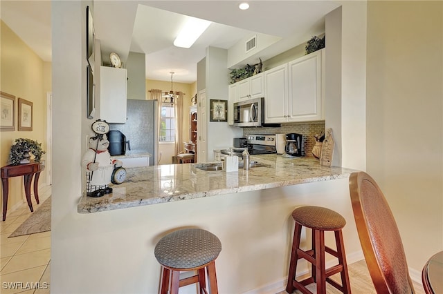 kitchen with kitchen peninsula, decorative light fixtures, stainless steel appliances, and white cabinets