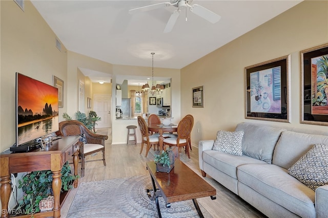 living room with ceiling fan with notable chandelier and light wood-type flooring