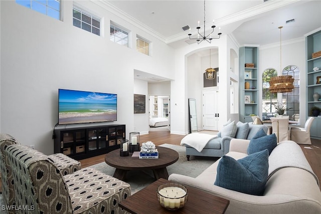 living room with an inviting chandelier, hardwood / wood-style floors, a towering ceiling, ornamental molding, and built in shelves