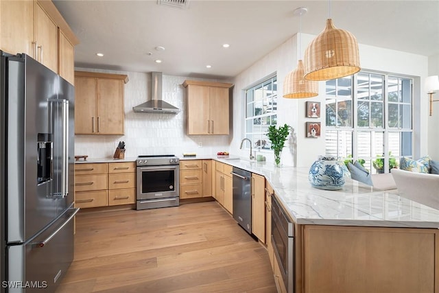 kitchen with stainless steel appliances, wall chimney range hood, pendant lighting, and light brown cabinetry