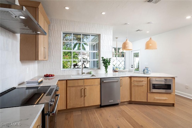 kitchen featuring pendant lighting, wall chimney range hood, sink, appliances with stainless steel finishes, and light wood-type flooring