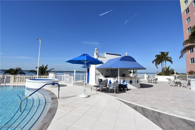 view of pool featuring a patio area, a water view, and a bar