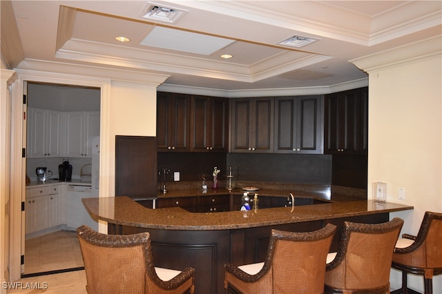 kitchen with a kitchen breakfast bar, a raised ceiling, kitchen peninsula, white dishwasher, and decorative backsplash