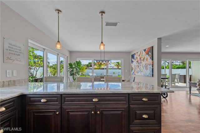 kitchen with dark brown cabinetry, light stone counters, and decorative light fixtures