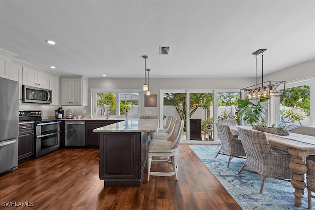 kitchen with dark wood-type flooring, appliances with stainless steel finishes, light stone counters, white cabinets, and a kitchen bar