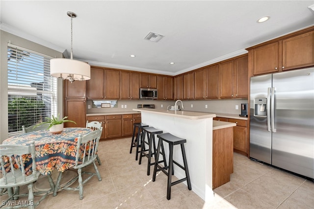 kitchen featuring stainless steel appliances, a center island with sink, hanging light fixtures, light tile patterned floors, and crown molding