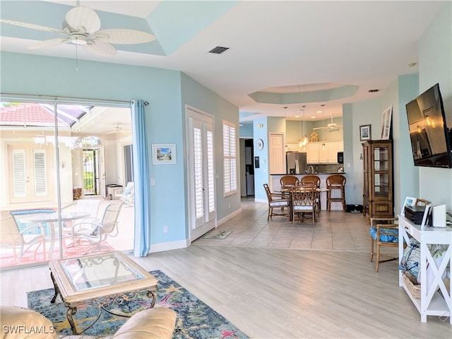 living room featuring a raised ceiling, ceiling fan, and light wood-type flooring