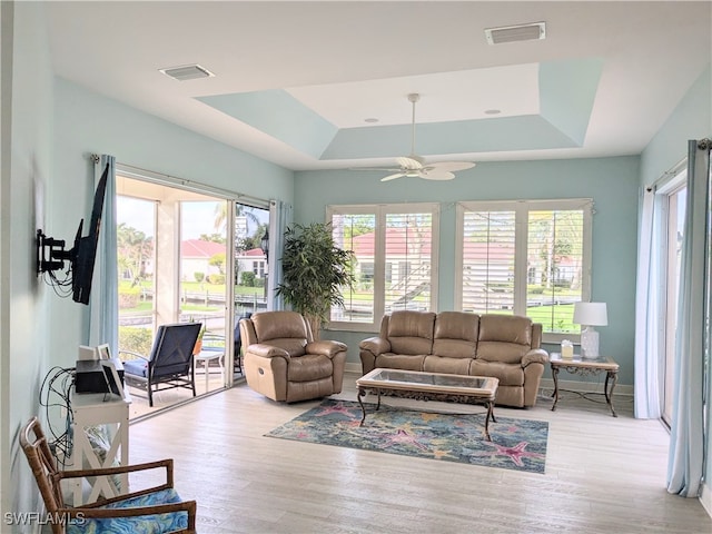 living room with a wealth of natural light, ceiling fan, a raised ceiling, and light wood-type flooring