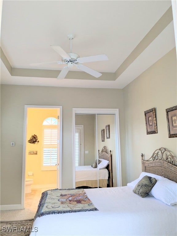 bedroom with light carpet, ensuite bathroom, a raised ceiling, ceiling fan, and a closet