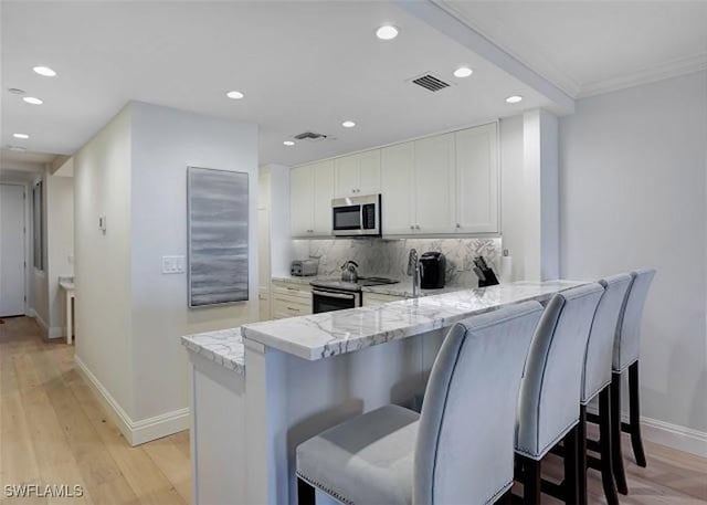 kitchen with kitchen peninsula, backsplash, stainless steel appliances, and white cabinets