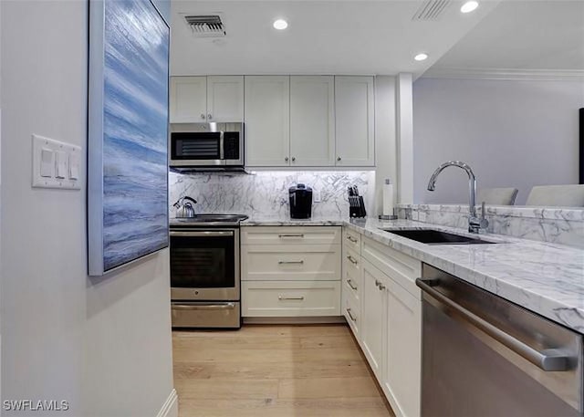 kitchen featuring white cabinets, sink, appliances with stainless steel finishes, light hardwood / wood-style floors, and light stone counters