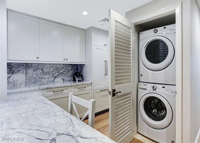 laundry area featuring stacked washer and dryer and light hardwood / wood-style flooring